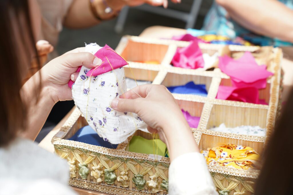 Hands sewing a piece of fabric with vibrant swatches in a wicker box.